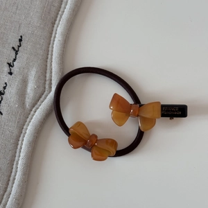 Détail de la barrette à nœud en résine ambrée et de l'élastique avec texte gravé