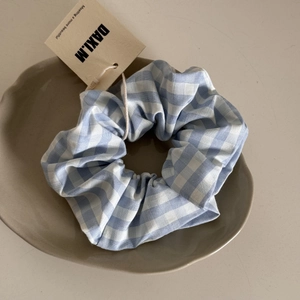 Close-up of blue and white gingham hair scrunchie with brand tag on ceramic tray