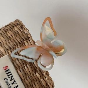 Macro view of marbled orange and blue acetate butterfly hair clip with metal duckbill base