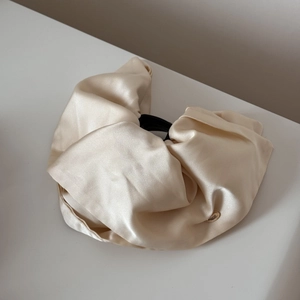 Macro shot of cream satin hair scrunchie with silky fabric texture and gold brand charm