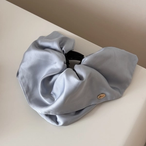 Detailed macro view of light blue satin fabric texture and golden metal logo on the hair claw