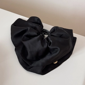 Detail of elegant black satin bow hair claw with gold metal wings logo plate