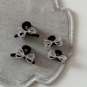 Detailed set of four black hair clips with elegant silver bead woven bows on a grey textured mat