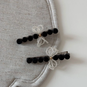 Detail of beaded bow hair clips with black multifaceted beads on a textured mat