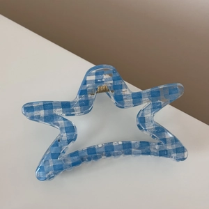 Detail shot of a star shaped hair claw clip featuring blue gingham pattern and gold spring