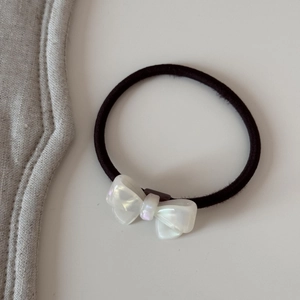Gros plan d'un élastique à cheveux noir avec un nœud en résine nacrée blanche élégant