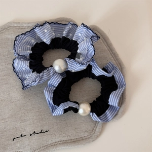 Détail du chouchou à rayures bleues avec une grande perle blanche sur tissu gris