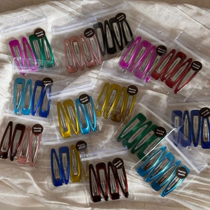 Detail of colorful BB hair clips in transparent packaging with branded labels on linen