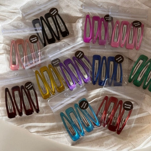 Set of four glossy metallic teardrop hair clips in vibrant colors on soft linen background