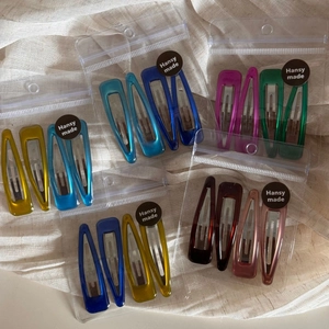 Close-up of assorted colorful 4-piece hair clip sets in transparent packaging on beige fabric