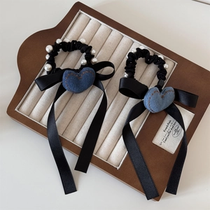 Dettaglio di elastico in raso nero con cuore in denim, perle bianche e lunghi nastri