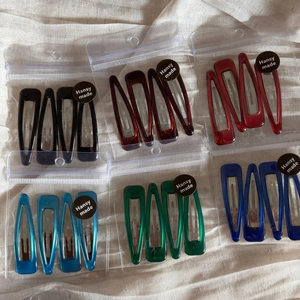 Close-up of assorted water-drop hair clips on beige linen background in a pack of four