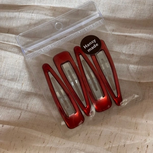 Set of four red metal snap hair clips in transparent packaging on a soft fabric background