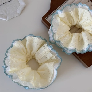 Detailed embroidery on light yellow lace scrunchies with blue scalloped edges