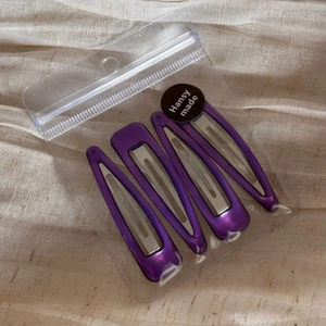 Close-up of 4 purple metal BB hair clips in transparent packaging on beige fabric