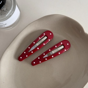 Detail view of red and white polka dot metal BB hair clips on a ceramic tray