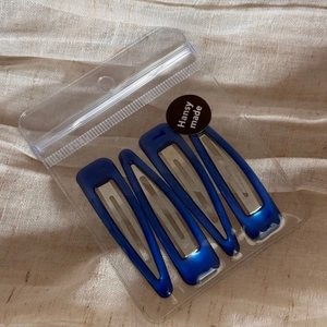 Set of 4 blue metal hair clips in transparent plastic packaging on beige fabric