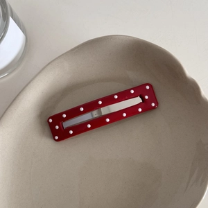 Close-up of a red leather polka dot hair clip on a beige ceramic plate