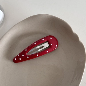 Detailed view of a red and white polka dot BB hair clip on a ceramic tray