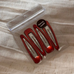 Detail view of four glossy dark red minimalist hair clips in branded transparent packaging