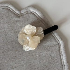 Detail of elegant cream acetate flower hair clip with pearl center on linen surface