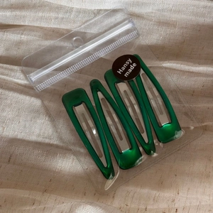 Set of four shiny green triangular hair clips in transparent bag with a black seal sticker