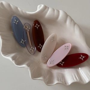 Detail of six colorful oval resin hair clips with rhinestones in a white shell dish