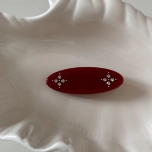 Close-up of vintage oval red hair clip with rhinestone star patterns on a shell tray