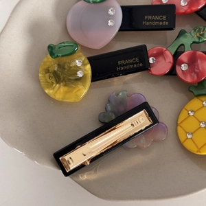 Détail de barrettes à cheveux en acétate avec fruits et strass sur un plateau
