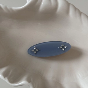 Detailed view of an oval blue matte hair clip with delicate rhinestone flower accents