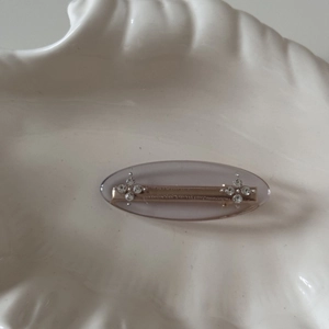 Detail of grey oval hair clip featuring rhinestone flower accents on a shell plate