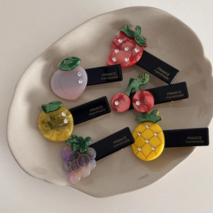 Détail de barrettes en acétate sur le thème des fruits avec strass sur assiette blanche