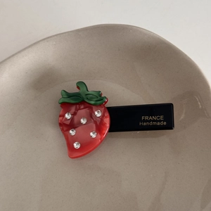Détail de la pince à cheveux fraise en acétate avec strass brillants et lettrage doré fait main