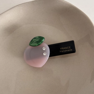 Détail d'une pince à cheveux pêche en acrylique rose avec feuille verte et strass