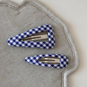 Detailed view of blue and white gingham fabric hair clips on a linen surface