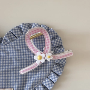 Détail d'une pince à cheveux à carreaux roses avec fleurs blanches et centres jaunes