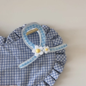 Détail d'une pince à cheveux à carreaux bleus et fleurs blanches sur coussin en cœur