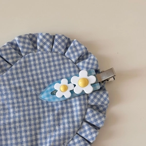 Vue détaillée d'une pince à cheveux à carreaux avec fleurs blanches sur tissu bleu