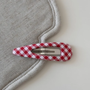 Detail of red and white gingham fabric texture on a teardrop-shaped metal BB hair clip