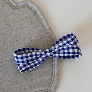 Dettaglio del fermaglio per capelli con fiocco vichy blu e bianco su base in lino