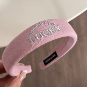 Detailed embroidery of LUCKY letters on a pink fabric headband with a handmade tag