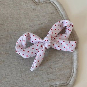Détail d'une pince à cheveux en tissu blanc à pois rouges avec une finition texturée