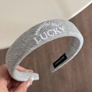Detailed close-up of grey knitted sponge headband with white Lucky embroidery and tag