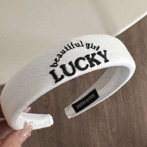 Detailed close-up of white sponge headband with black LUCKY and beautiful girl embroidery