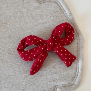 Détail d'une pince à cheveux à nœud rouge à pois blancs sur un fond minimaliste