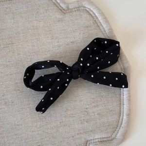 Détail d'une pince à cheveux à nœud avec pois noirs et blancs sur fond gris texturé