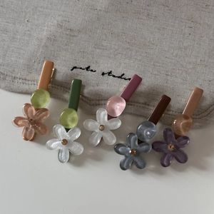 Set de cinco pinzas para el pelo con flores de resina de colores y pedrería en fondo beige