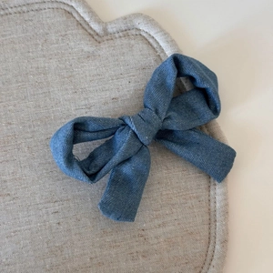 Détail d'une pince à cheveux nœud en denim bleu avec texture sergée sur tapis beige