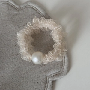 Dettaglio dell'elastico per capelli in rete bianco crema con pieghe e perla bianca