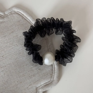Dettaglio di un elastico per capelli in rete nera con una grande perla bianca decorativa